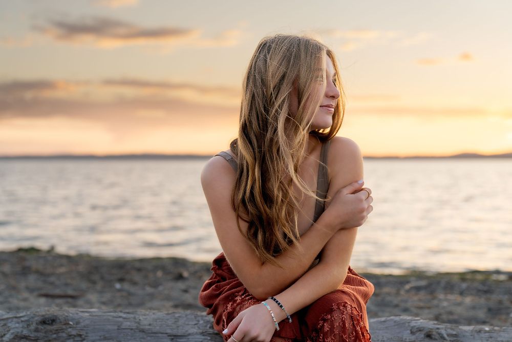 Person sitting on rocky beach at sunset with arms crossed by Filling the Frame Photography's at Lopez Island in San Juan Islands.