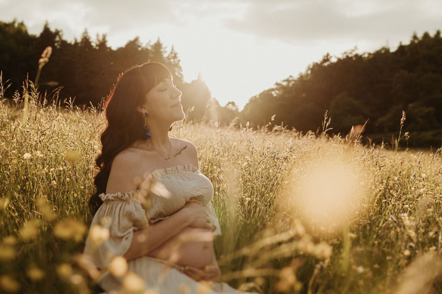 Ethereal sunset photo in a golden field with sunflare and forest silhouettes.