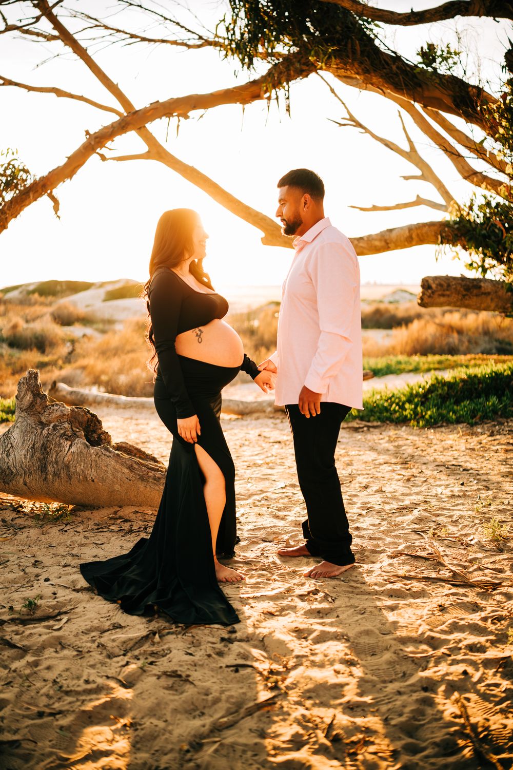Maternity session in Pismo Beach, Ca. Mom and dad standing, facing eachother in front of the sunset.