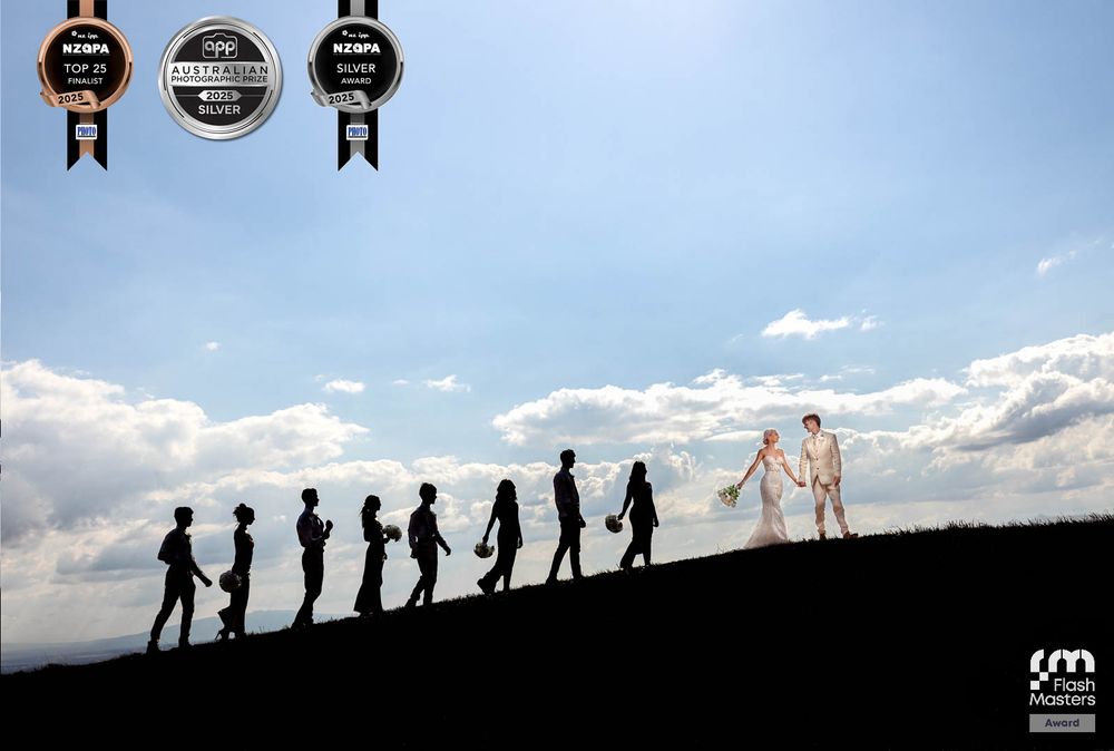 Award winning wedding image couple under midday sun against a blue backdrop sky with their wedding party silhouette behind them award badges