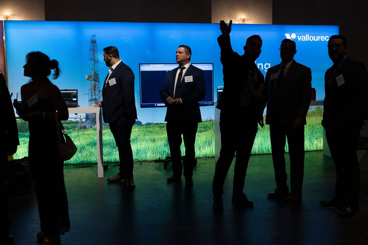 Silhouettes of people against blue-lit display screens at corporate event.