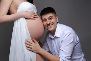 Smiling man in white shirt listening to pregnant woman's belly during maternity photo shoot.