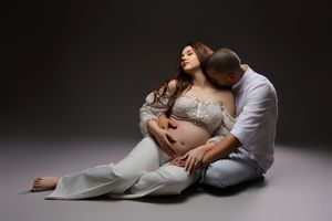 A series of intimate maternity photos showing a couple in white clothing posing together against a dark background.