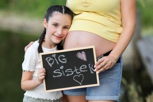 Outdoor maternity announcement photo with chalkboard signs in natural lighting.