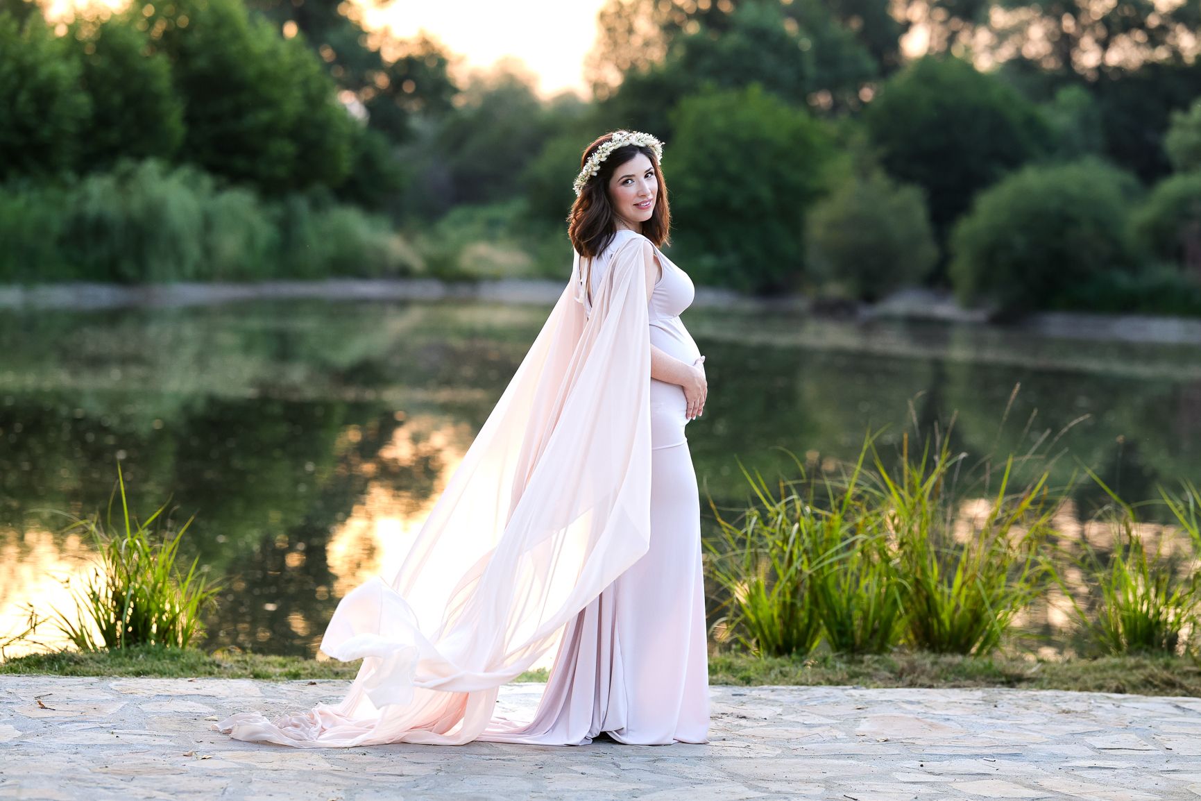 A flowy pink maternity gown catches the sunset light in an outdoor nature session.