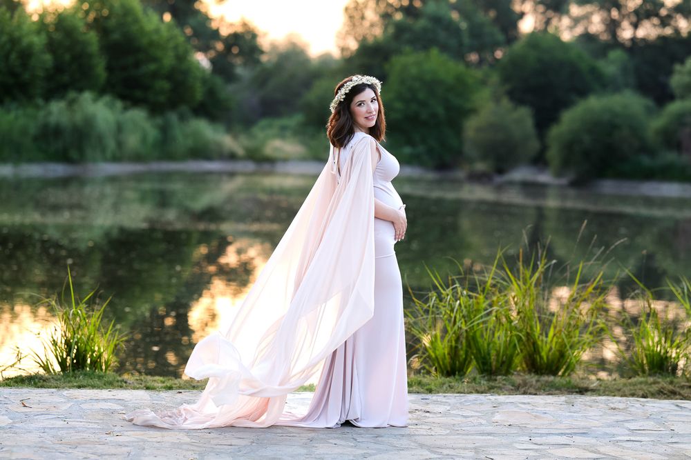 A flowy pink maternity gown catches the sunset light in an outdoor nature session.