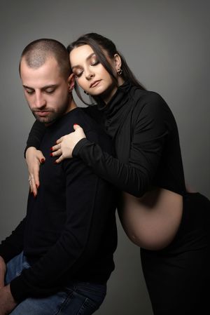 Intimate maternity portrait of couple dressed in black against gray background.