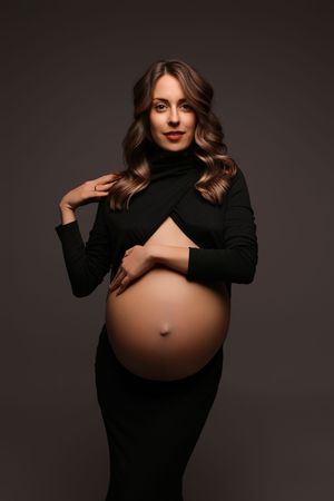 Artistic maternity photo sequence showing a woman in black against dark background revealing growing baby bump.