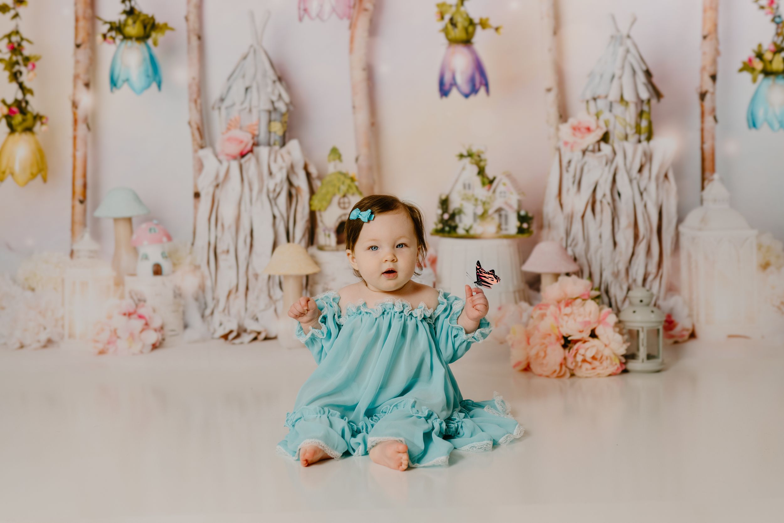 A floral studio session setup with pink and aqua fabrics, colorful flowers, and whimsical decorative elements.
