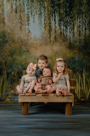 Multiple babies in light pink outfits lying together on a wooden bench against a moody outdoor backdrop.