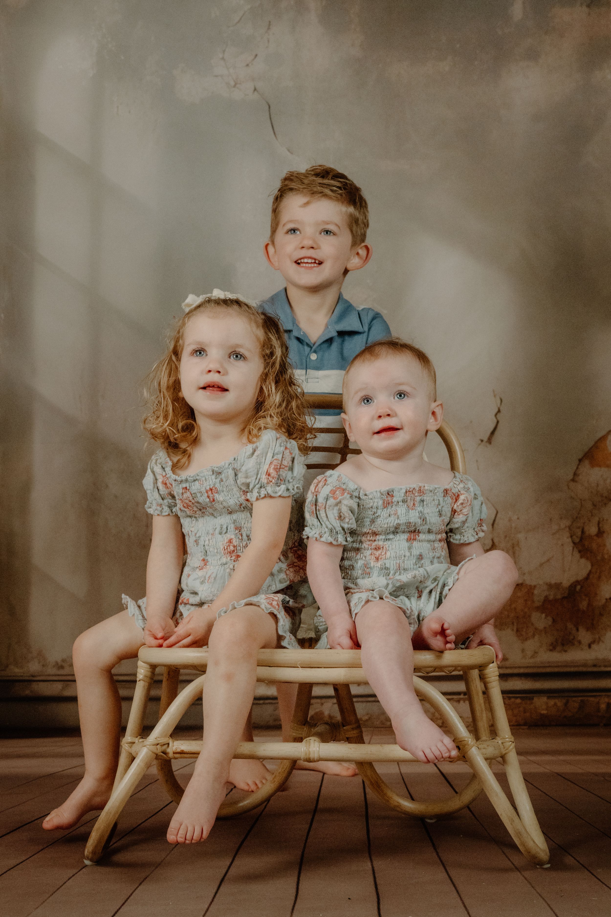 Vintage-style portrait series of two young children sitting together in matching outfits on wooden furniture.