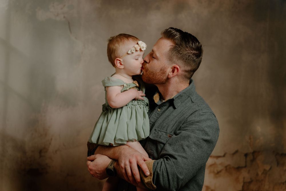 A parent and small child share multiple intimate embracing moments against a dark rustic backdrop.