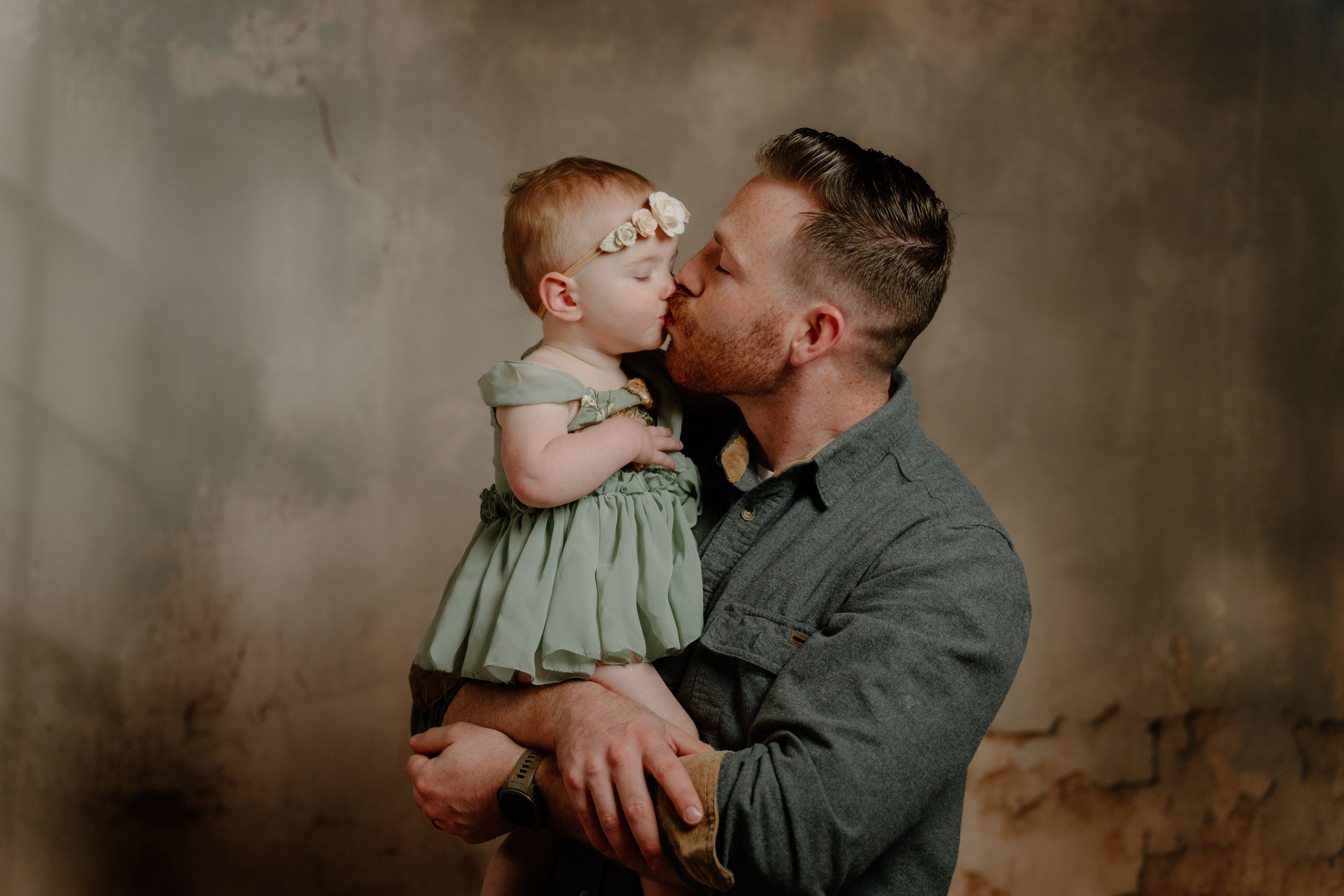 A parent and small child share multiple intimate embracing moments against a dark rustic backdrop.
