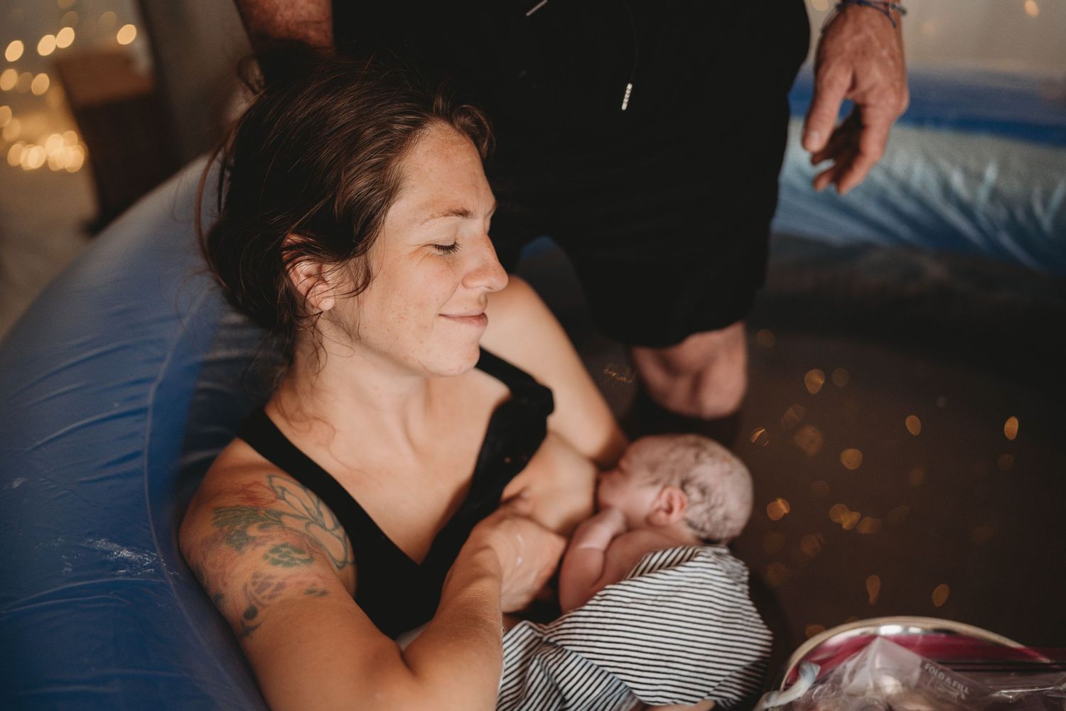 Intimate Palm Beach birthing scene with newborn baby in dimly lit room with string lights.