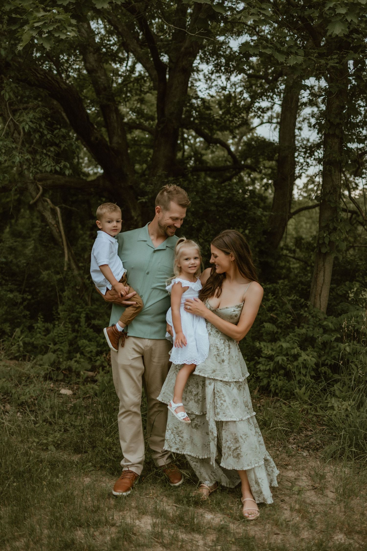 A family shares a tender moment together while posing in a wooded outdoor setting during golden hour.