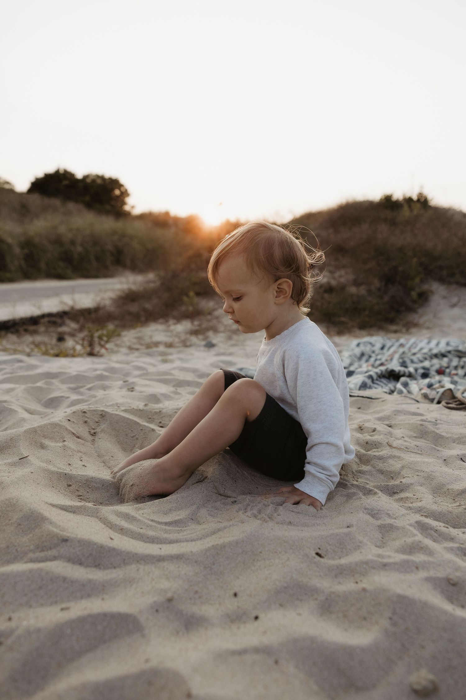 Toddler sitting barefoot in golden sand at sunset on a peaceful beach at dusk. Horseneck Beach Westport Ma. Miranda Photo & Co