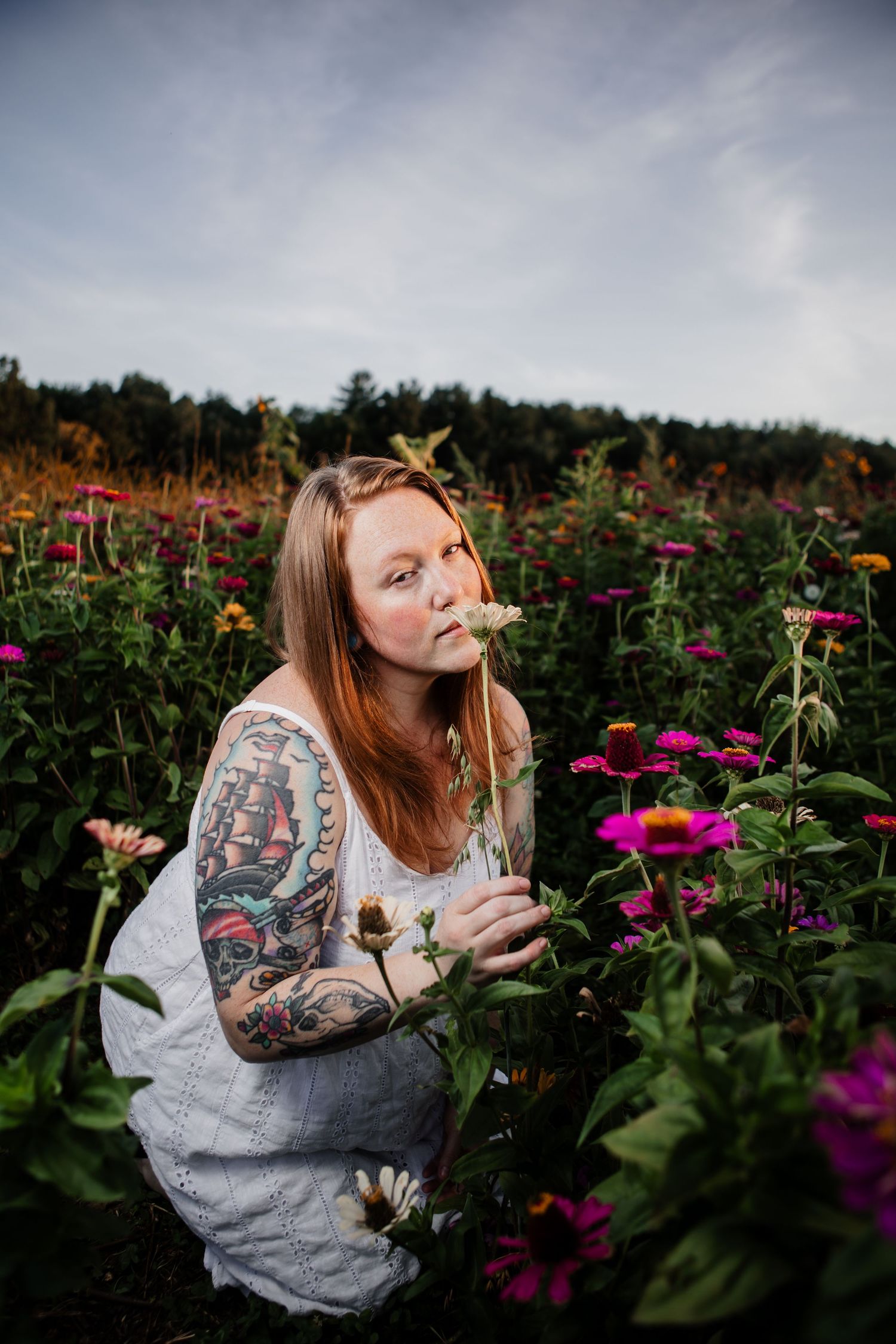 Person with tattoos smelling flowers in a vibrant garden of pink zinnias.