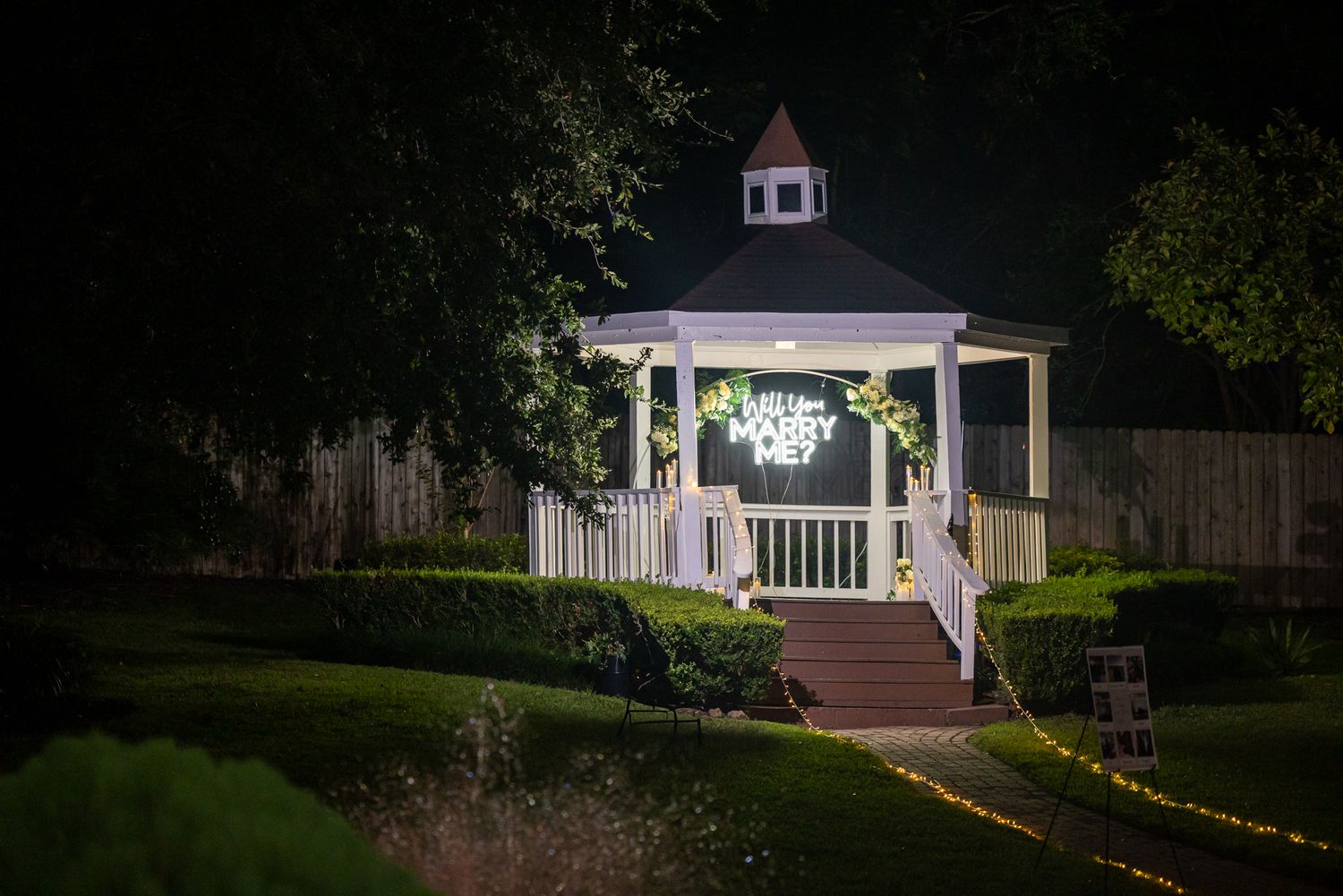 Large white 'MARRY ME' letters displayed on grass with decorative elements and a gazebo in background.