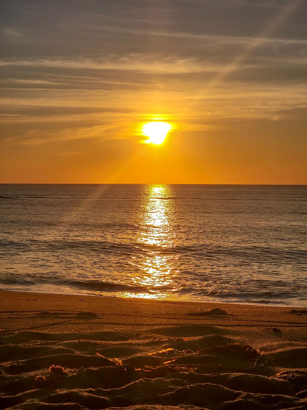 Golden sunset over calm ocean waves with warm orange sky reflecting on wet sandy beach.
