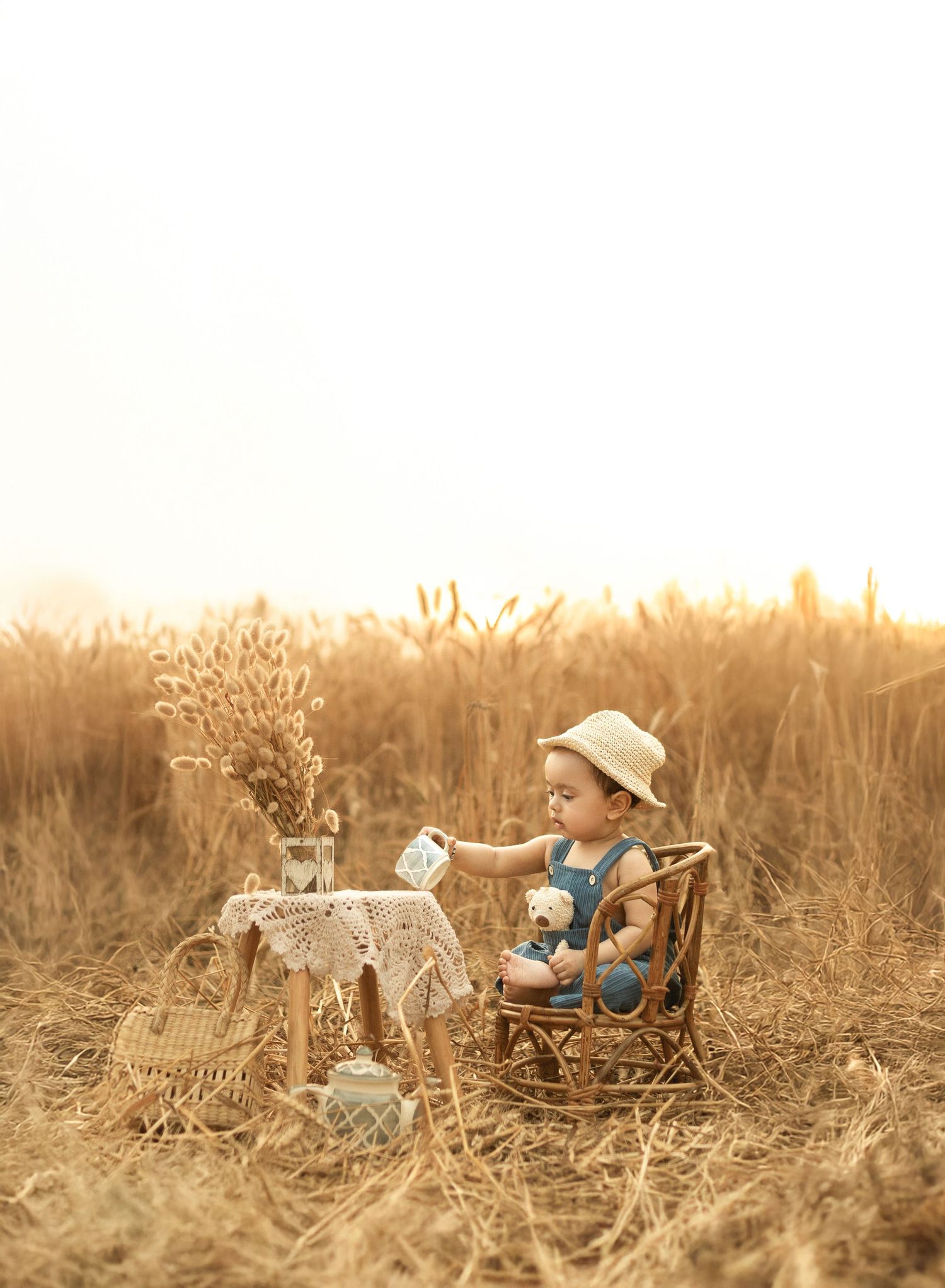 A dreamy golden sunset scene showing a tiny table setup and chair in a rustic wheat field.