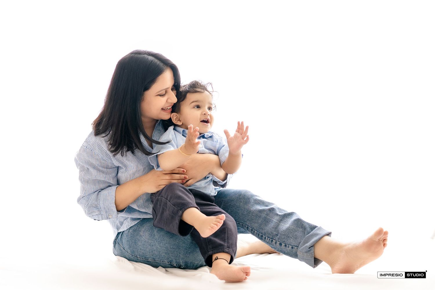 Parent and child wearing casual denim clothes laugh and play together while sitting on white background.