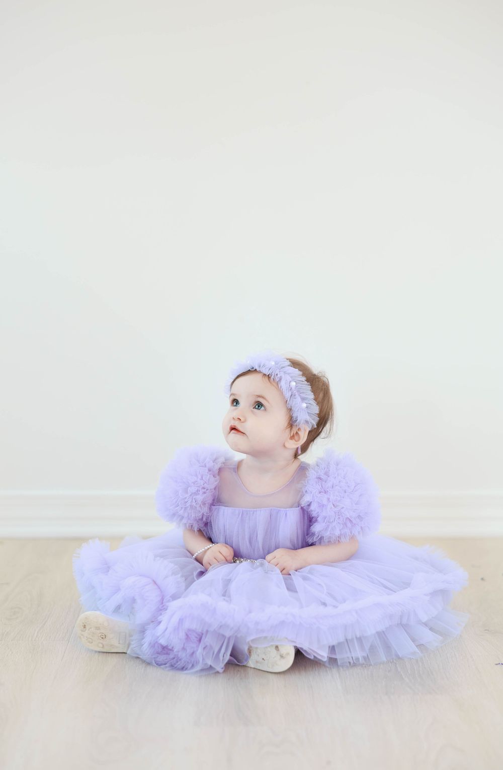 A small child in a lavender tulle dress poses gracefully in a ballet-inspired photo series against a white backdrop.