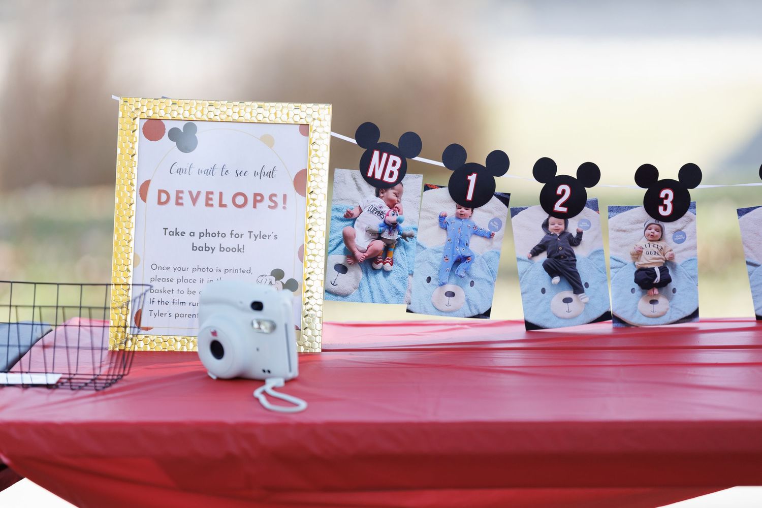 Mickey Mouse themed first birthday party display with monthly baby photos and Instax camera.