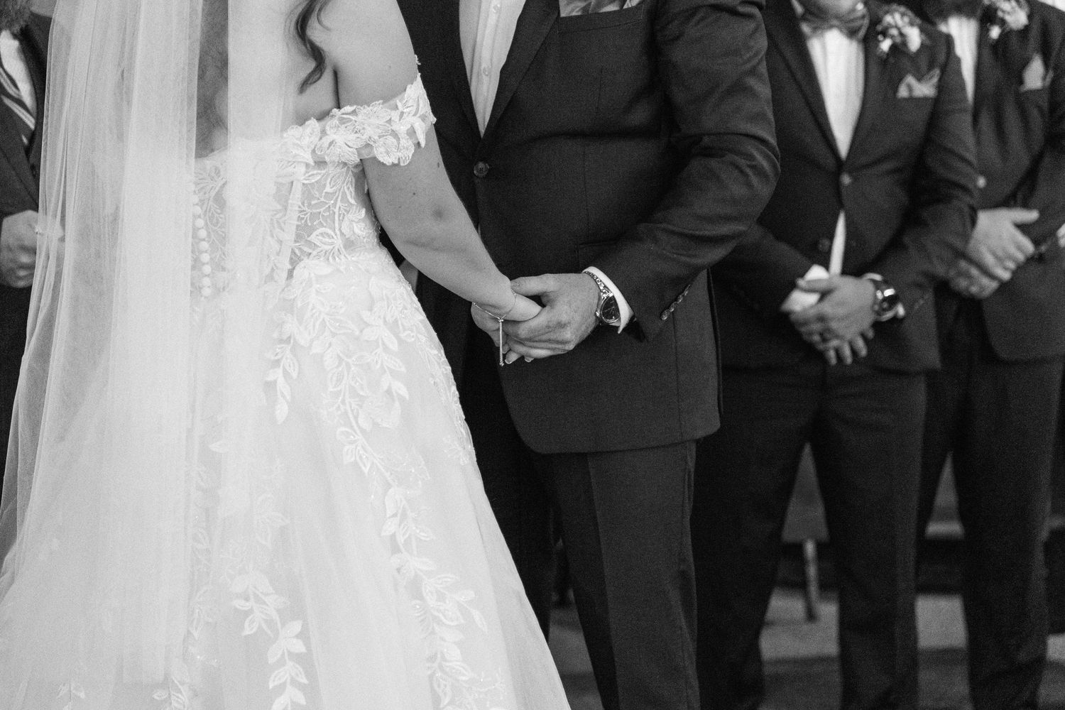 Wedding ceremony with bride and groom holding hands and groomsmen standing in the background.