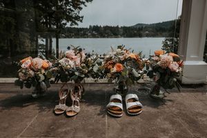 Wedding bouquets and bridal shoes arranged on a patio overlooking a serene lake.
