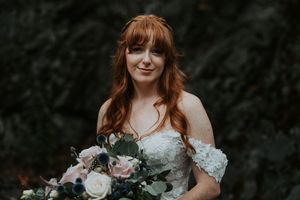 Red-haired bride smiles softly holding a lush pink and navy floral bouquet.