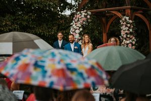 Outdoor wedding ceremony with colorful umbrellas shielding guests from rain.