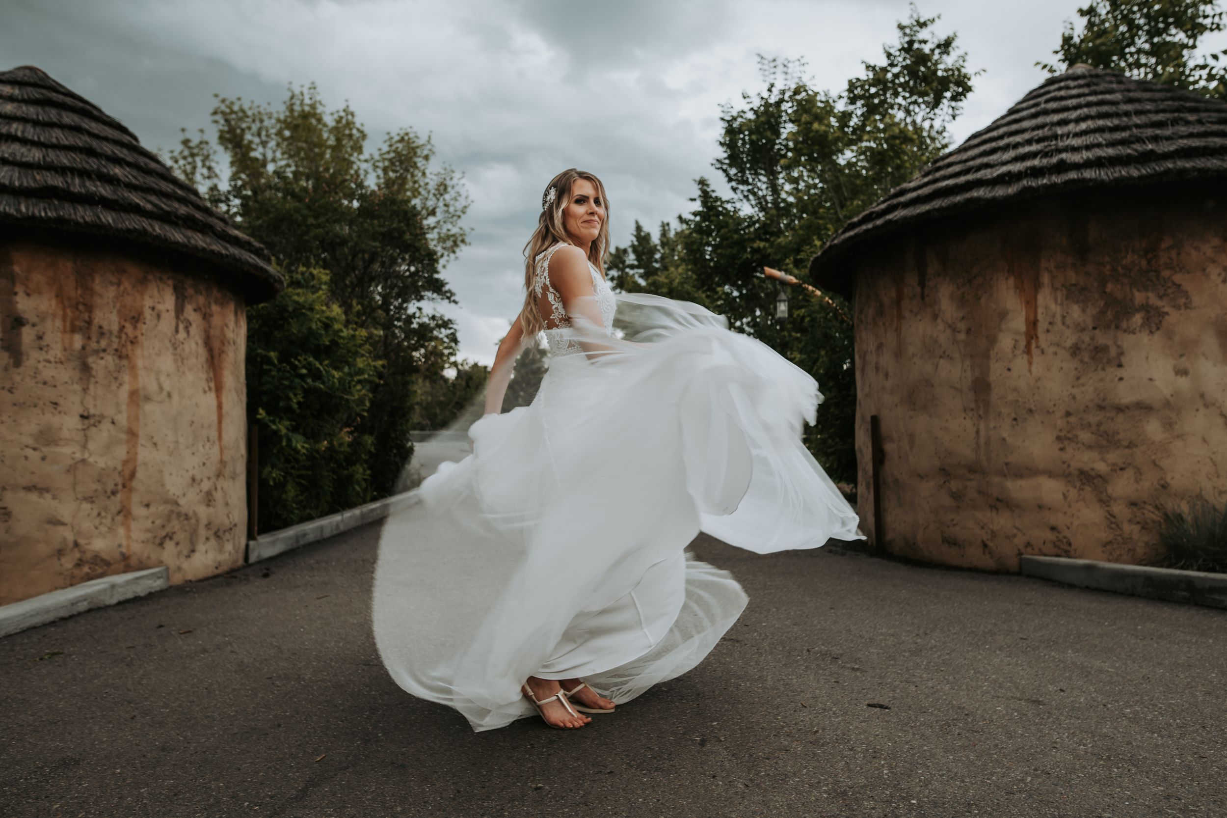 Bride twirling in flowing white wedding gown on rooftop with dramatic sky.