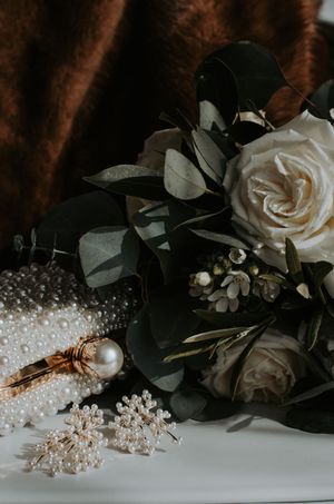 White roses and eucalyptus bridal bouquet beside pearl jewelry and hair accessories.