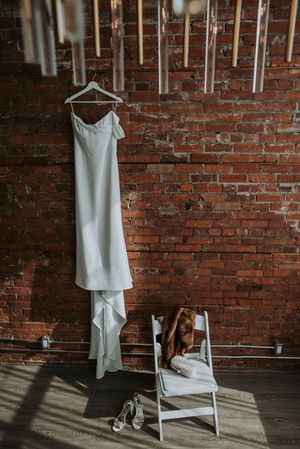 Minimalist white wedding dress hanging on a brick wall above heels and a fur stole.