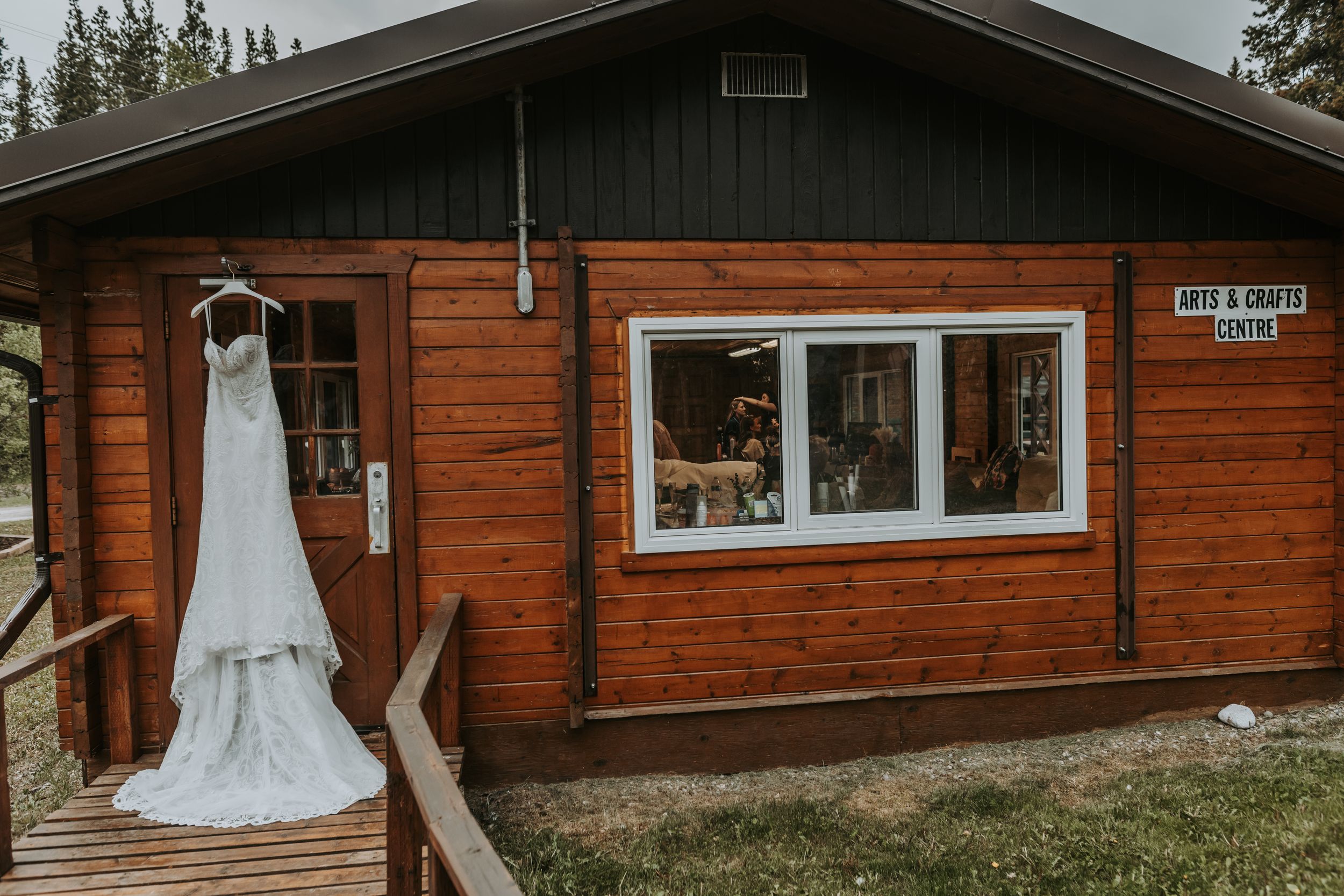 Wedding dress hanging outside a rustic log cabin arts and crafts centre in the woods.