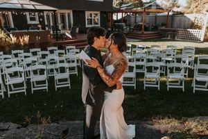 Bride and groom sharing a kiss in front of white ceremony chairs outdoors.