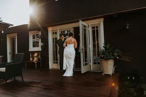 Bride and groom standing on a deck at sunset near French doors.