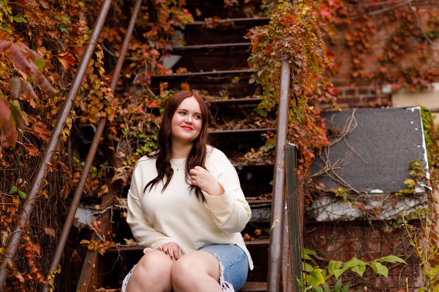 Neoga High school senior on a rusty stairwell, next to fall foliage, posing in white sweater, posing for Amber Helm Photography