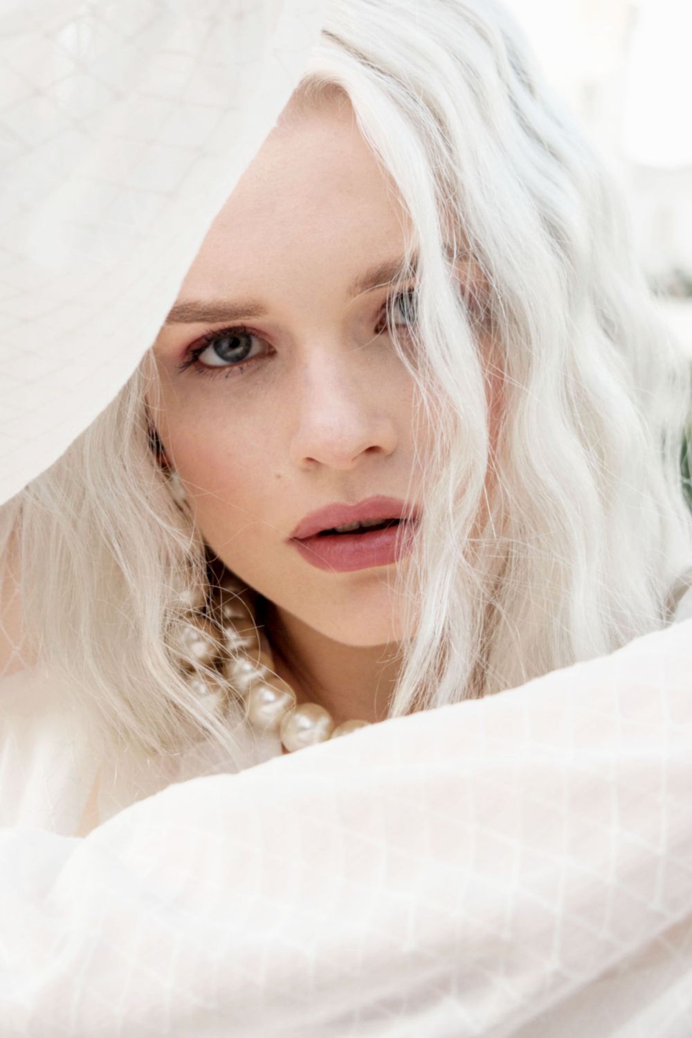 Ethereal portrait of a woman with platinum blonde hair, draped in white fabric, taken at a Cambridgeshire wedding love location. UK