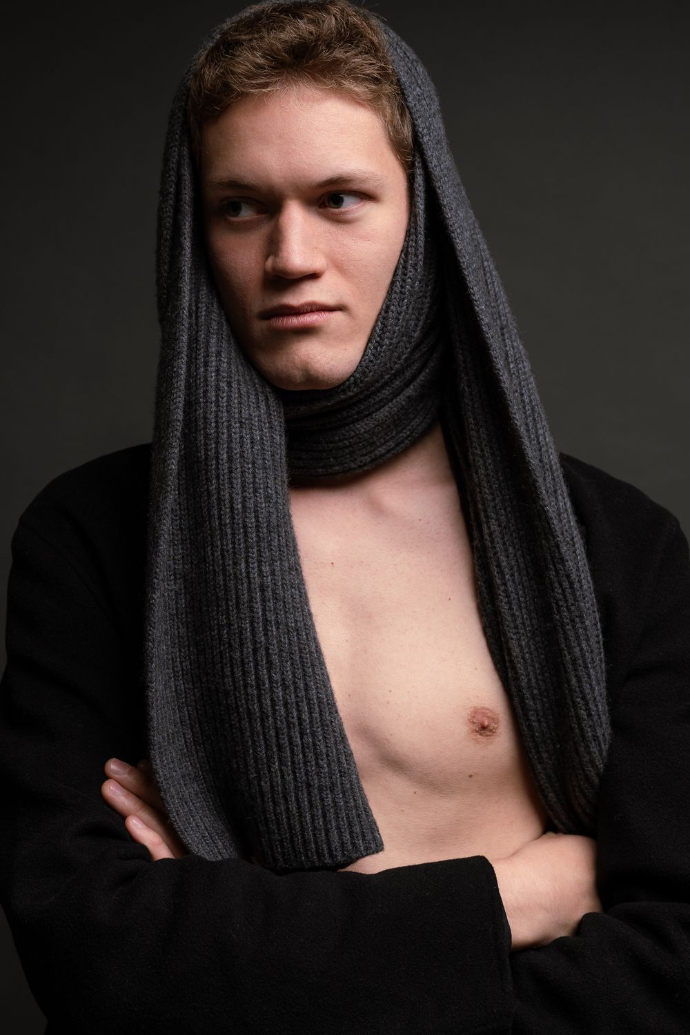 Dramatic portrait showing a man partially covered by a dark knit scarf against a dark background, Cambridge, UK