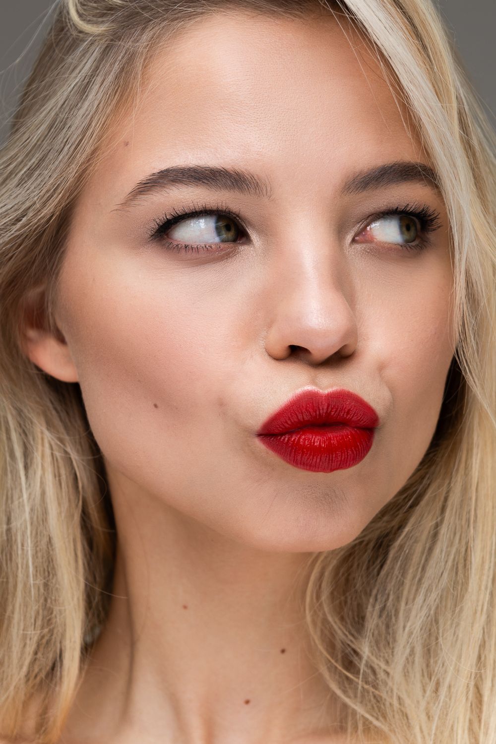 Close-up of a blonde woman with red lips, making a playful expression, shot in a London studio, UK