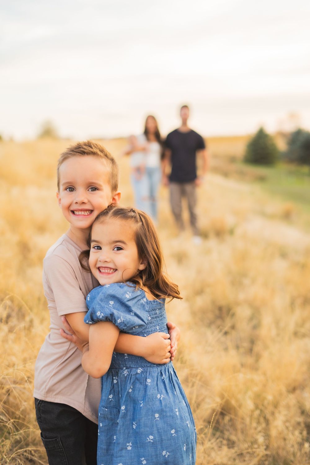 Children playing together in tall grass during golden hour photography session.
