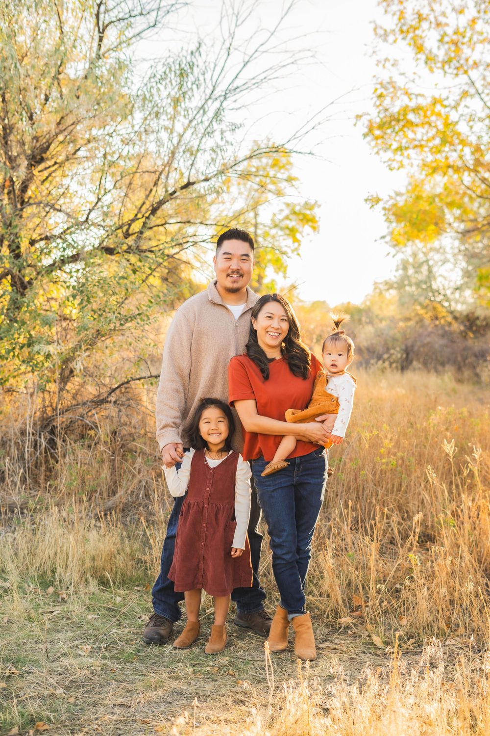 Family standing together in autumn field with golden light filtering through trees.