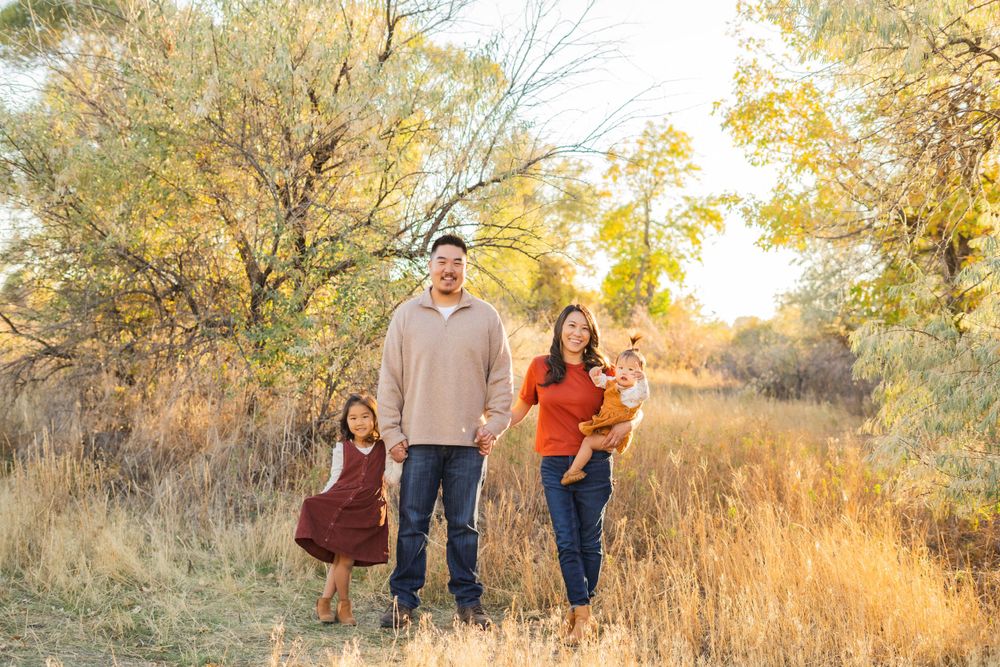 Family outdoor portrait in autumn field with golden grass and trees.