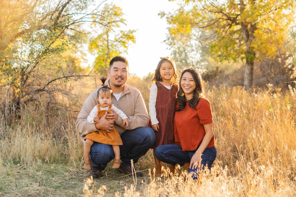 Family group portrait in warm autumn setting with golden grass and trees.