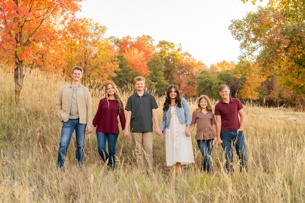 A group stands together in a golden autumn field with vibrant orange trees behind them.