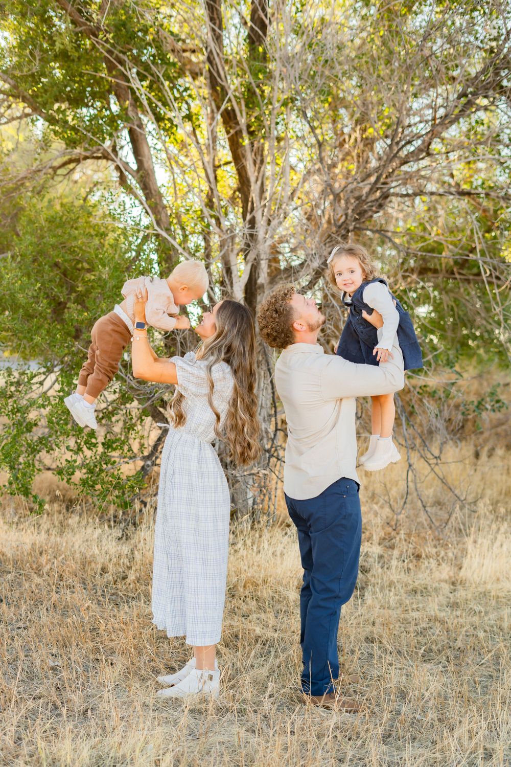 A family playfully lifts their children in the air while standing in a natural outdoor setting.