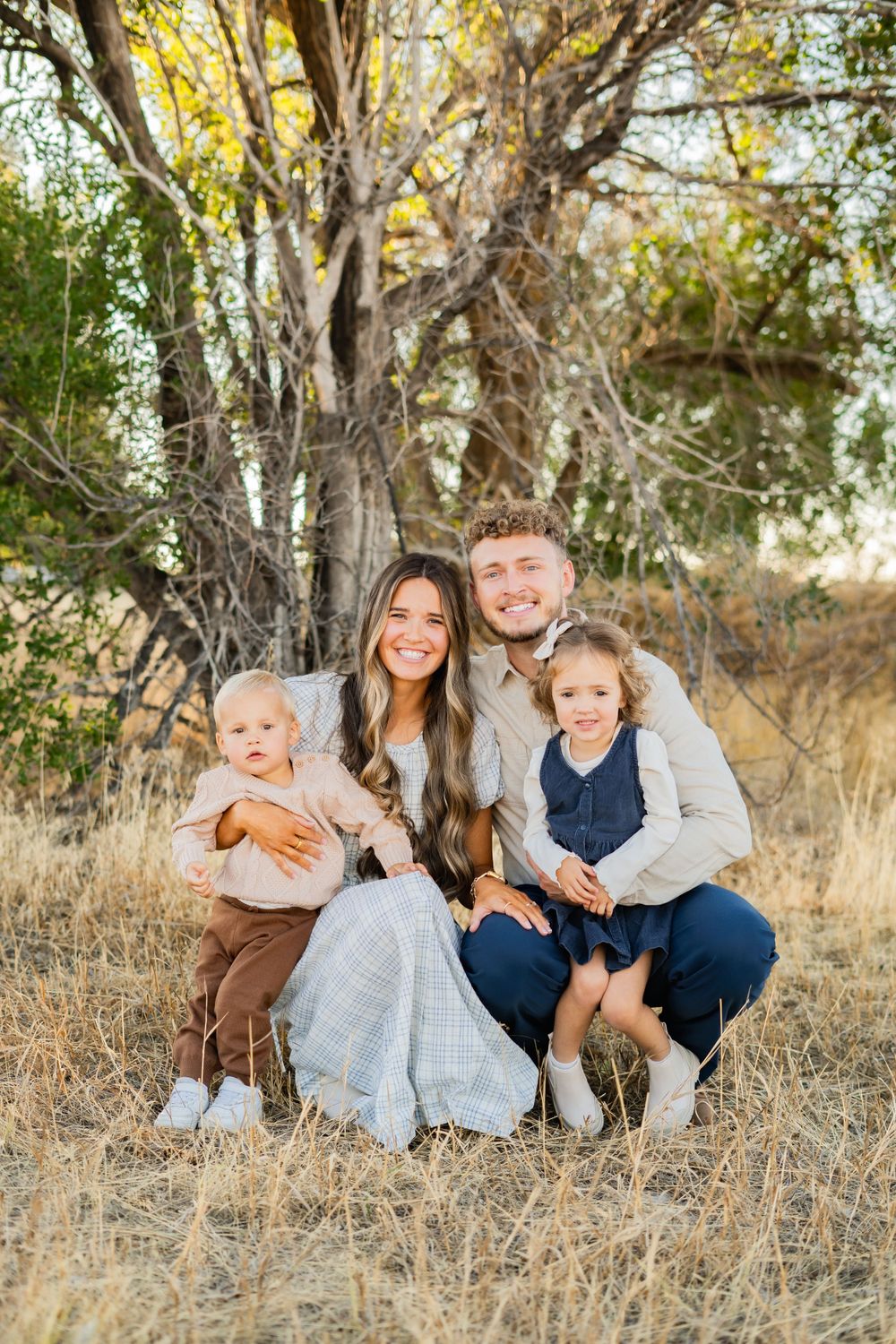 Family portrait session captured in a rustic outdoor setting with tall grass and trees.