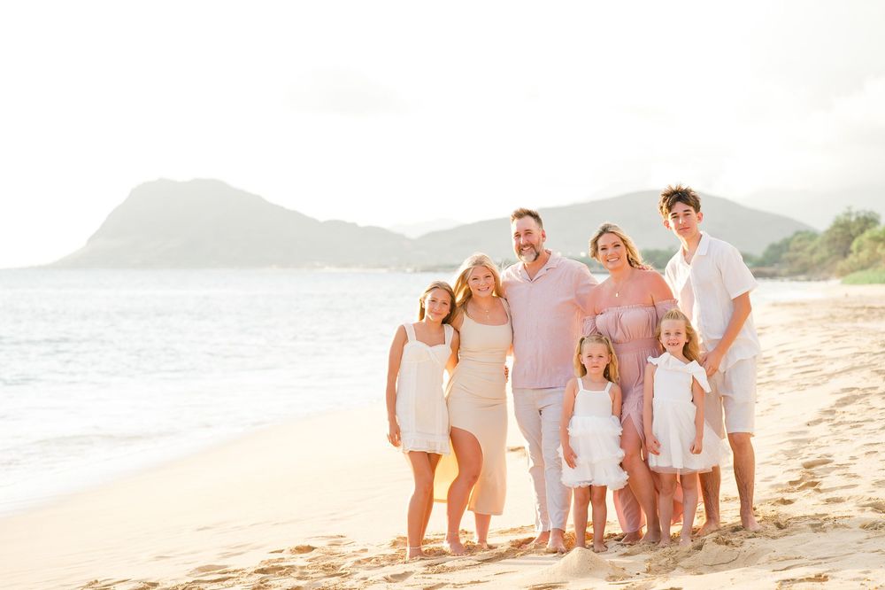 A family wearing white outfits poses together on a sandy beach at sunset.
