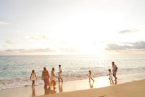 People walking along a scenic beach at sunset with waves crashing on the shore and warm golden light in the sky.